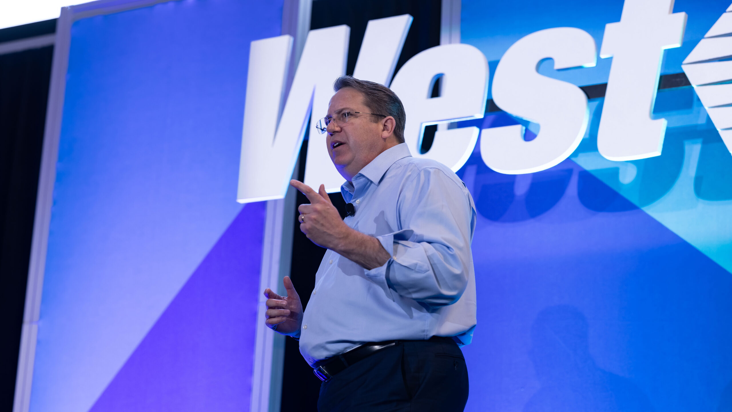 Speaker presenting on stage in front of the West logo
